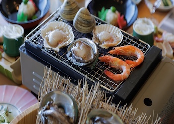 大洗ホテルの夕食で提供される海鮮浜焼き。卓上コンロの網で帆立・はまぐり・海老を焼いている