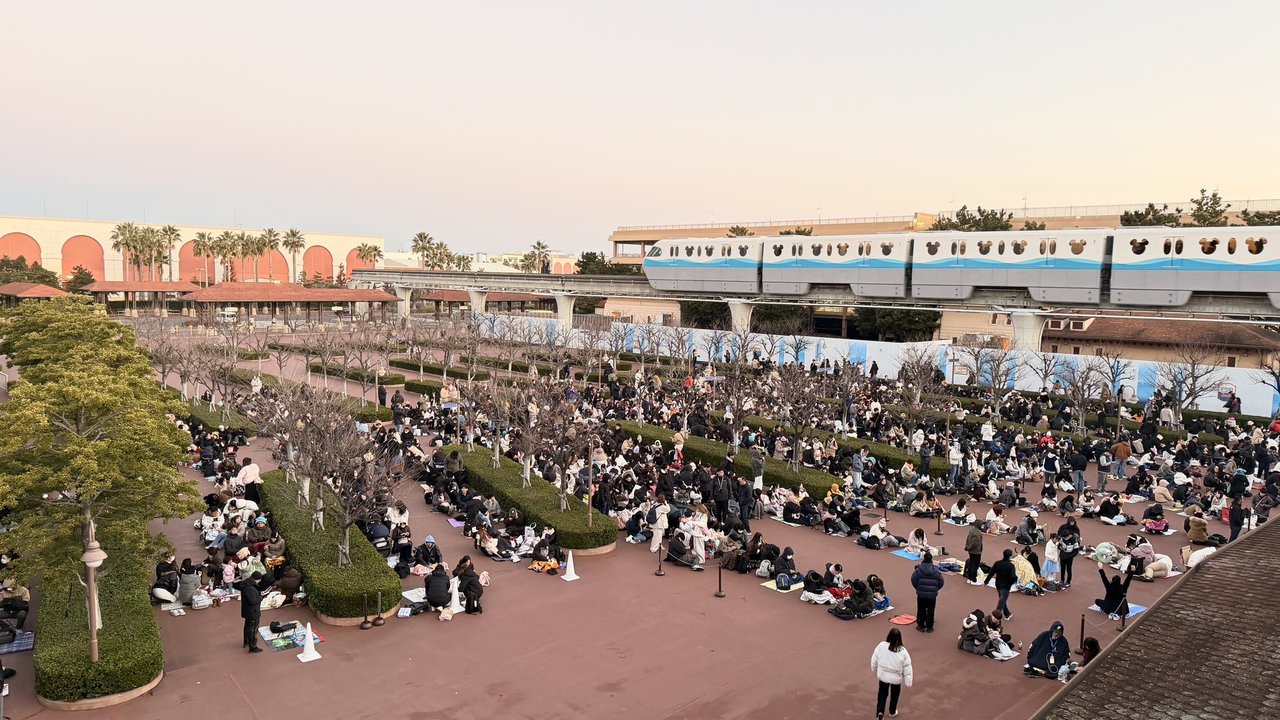 2025年12月30日の朝6時40分、ノースゲート前の広場で敷物を敷いて座り、入園を待つ大勢の人。上をディズニーリゾートラインが走る