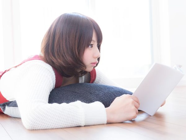床に寝転んで本を読む女性