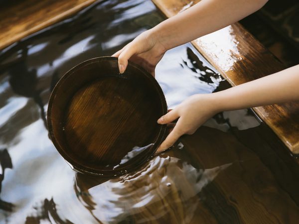 温泉の湯に木の湯桶を浸す手元
